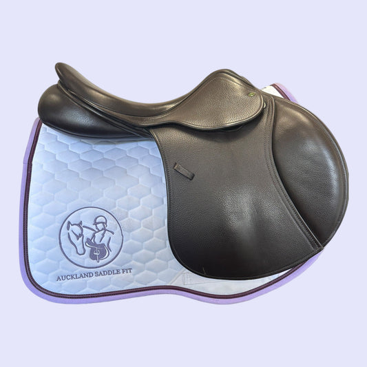 Brown leather saddle with a quilted blue pad on a light purple background