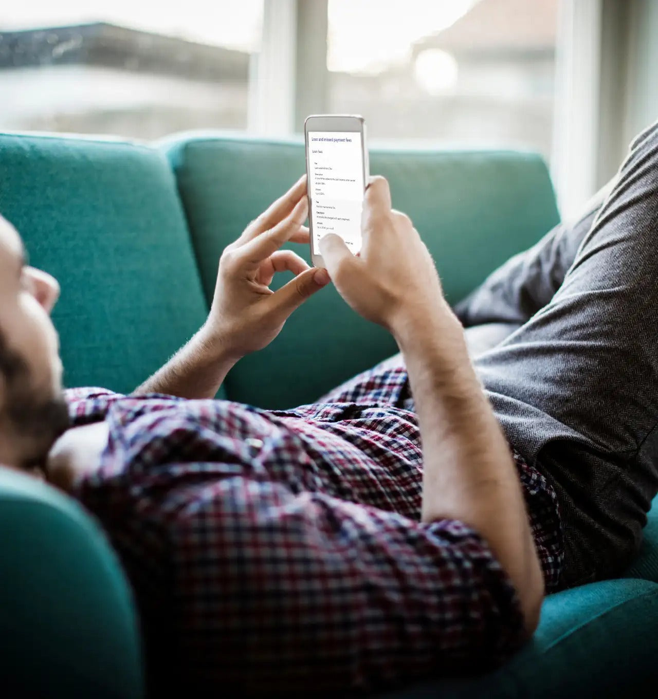 Person sitting on a teal couch using a smartphone.