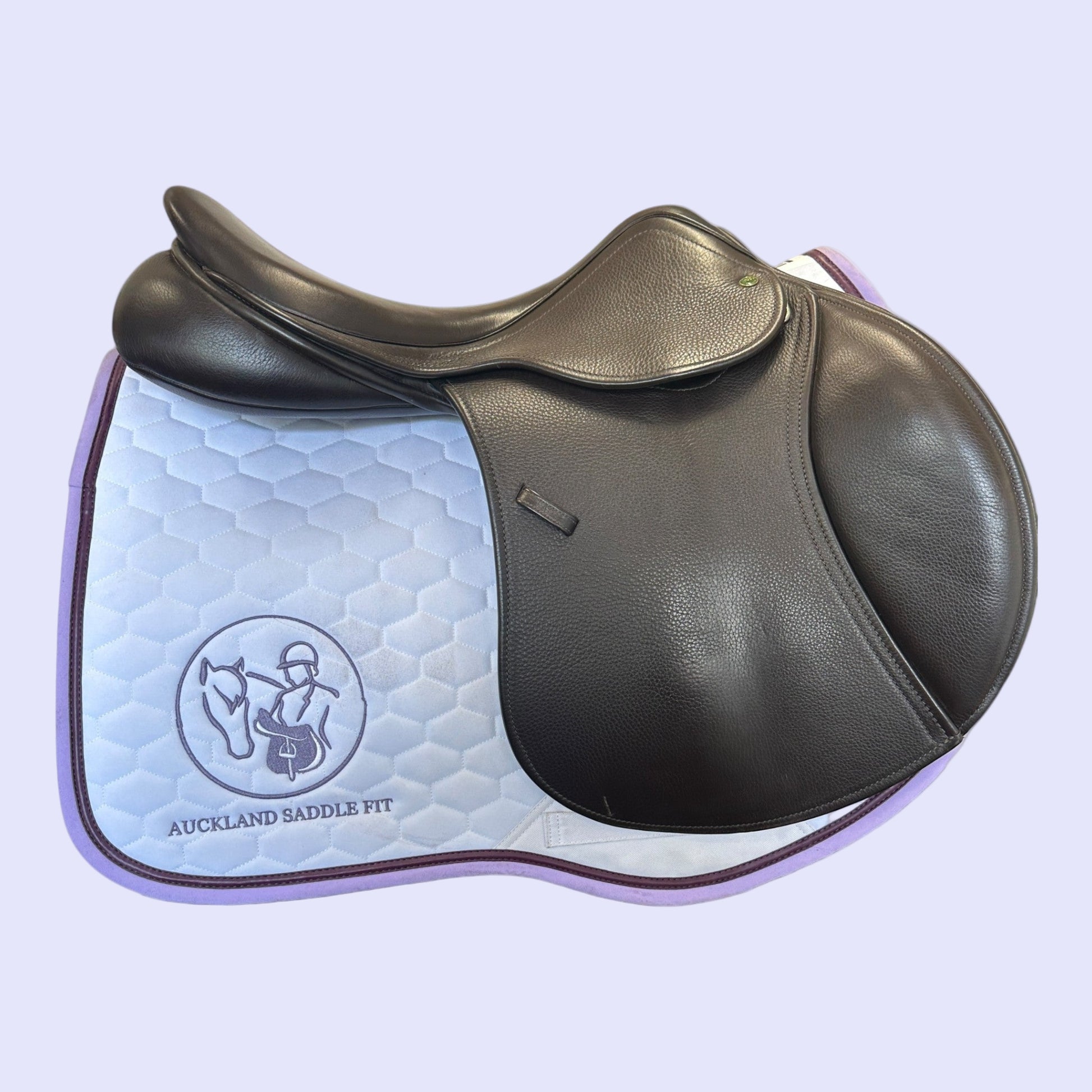 Brown leather saddle with a quilted blue pad on a light purple background